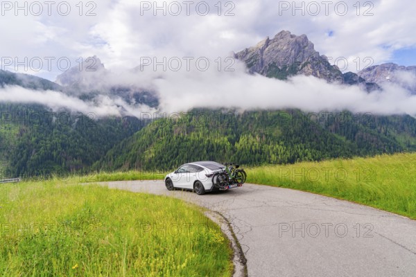 The car parked on a path in an impressive mountain landscape with fog and grass, electric car on holiday, Dolomites, South Tyrol, Dolomites, Italy, Europe