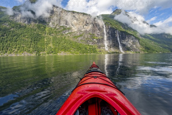 Kayak trip on the Geirangerfjord with waterfall The Seven Sisters, tip of a red kayak in the fjord, atmospheric fjord landscape with reflection, first person view, near Geiranger, Møre og Romsdal, Norway, Europe