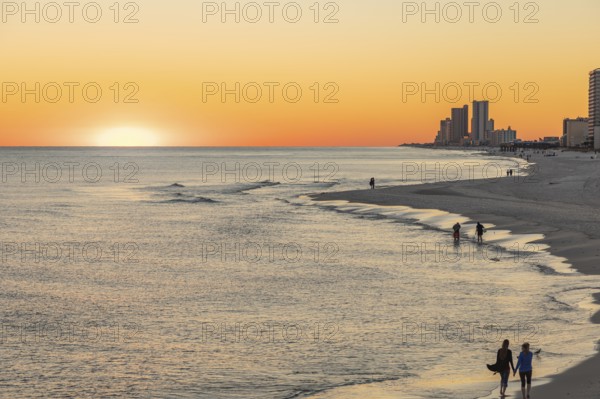 People walking and playing on the beach as the sun sets over the Gulf of Mexico at Gulf Shores, Alabama