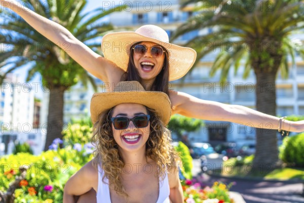 Two cheerful female friends are having fun during summer vacation, wearing sunglasses and straw hats
