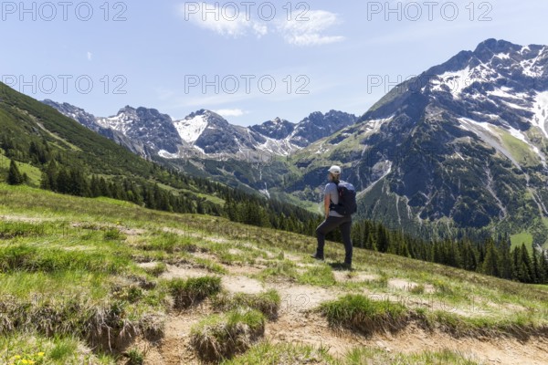 Hiker gazes at majestic snow-capped mountain peaks of the Alps in Kleinwalsertal, Austria, Europe