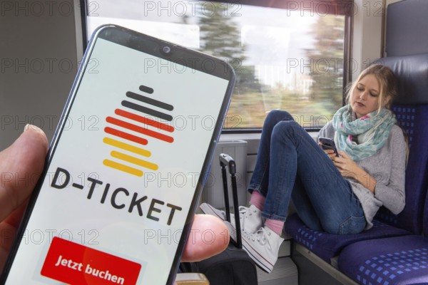(Photomontage) Logo of the Deutschlandticket on the smartphone, in the background a young woman on the train