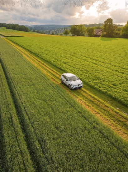 A car drives on a rural road through green fields, a village in the background, Deer E- CarSharing, Renault Megane electric car, Calw, Black Forest, Germany, Europe