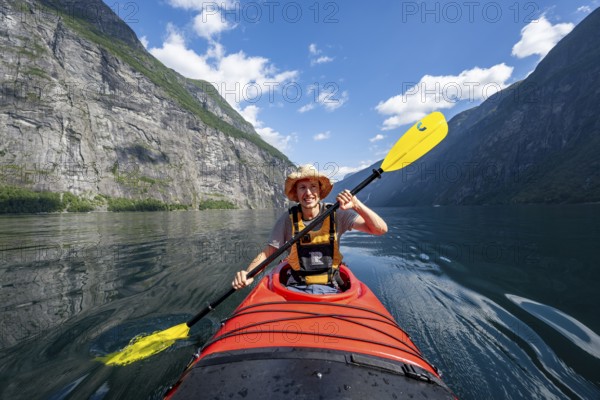 Kayak trip on the Geirangerfjord, young man paddling in red kayak, atmospheric fjord landscape, near Geiranger, Møre og Romsdal, Norway, Europe
