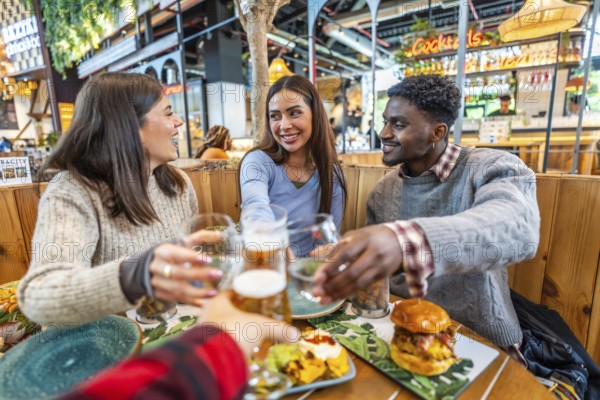 Group of cheerful multi ethnic friends toasting with beer and cocktails, enjoying meal together at food market