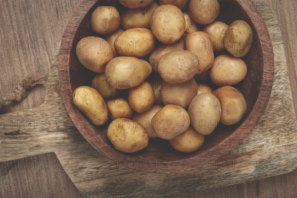 A bowl filled with small, freshly harvested potatoes sits on a rustic wooden cutting board, showcasing the earthy tones and natural textures of the produce