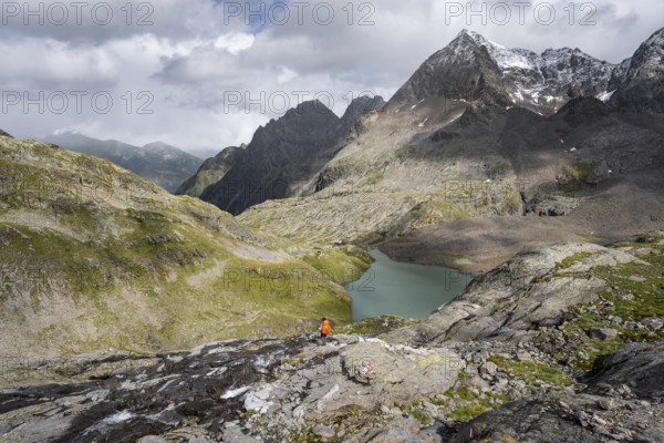 Mountaineer on a rocky hiking trail, view of the turquoise-blue mountain lake Großer Gradensee, behind her the summit of the Petzeck, Hoher Perschitzkopf and Kruckelkopf, Schober Group, Hohe Tauern National Park, Carinthia, Austria, Europe