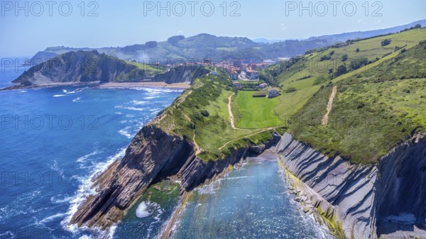 Aerial perspective captures the stunning beauty of zumaia's flysch cliffs meeting the vibrant blue ocean on a sunny summer day, Spain.