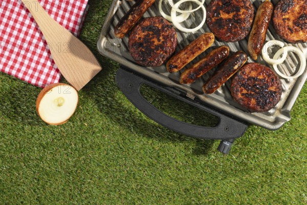Barbecue with sausages and burgers next to a red and white chequered cloth on a green lawn