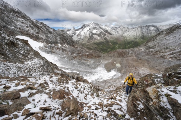 Mountaineer on a rope-secured climb in a steep rocky mountain landscape with fresh snow in summer, mountain peak Roter Knopf in the background, descent from the Hornscharte on the Wiener Höhenweg, Schober Group, Hohe Tauern National Park, Carinthia, Austria, Europe