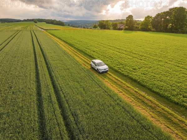 A car on a farm track between green meadows and under drifting clouds, Deer E- CarSharing, Renault Megane electric car, Calw, Black Forest, Germany, Europe