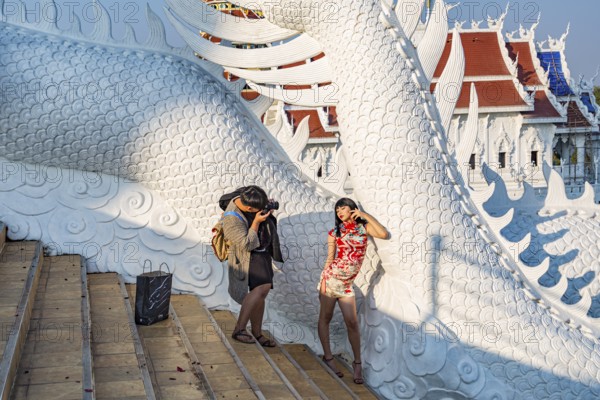 Photographer photographing young Thai woman on the steps of the Guan Yin (Goddess of Mercy) statue at Wat Huay Pla Kang Temple in Chiang Rai province of Northern Thailand