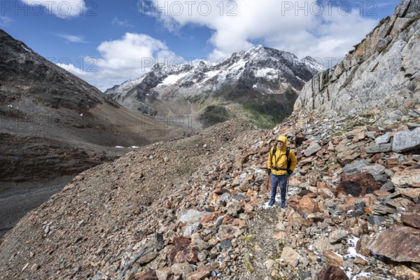 Mountaineer on hiking trail in steep rocky mountain landscape with fresh snow in summer, behind mountain peak Roter Knopf, descent from the Hornscharte on the Wiener Höhenweg, Schober group, Hohe Tauern National Park, Carinthia, Austria, Europe