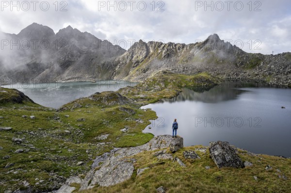 Mountaineer on a rock in front of mountain lakes Wangenitzsee and Kreuzsee, cloudy mountain peaks in the morning, Schober group, Hohe Tauern National Park, Carinthia, Austria, Europe