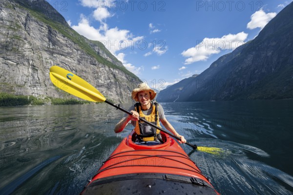 Kayak trip on the Geirangerfjord, young man paddling in red kayak, atmospheric fjord landscape, near Geiranger, Møre og Romsdal, Norway, Europe