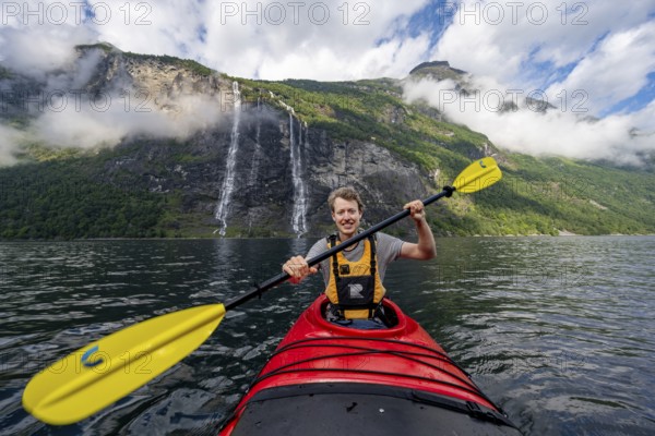 Kayak trip on the Geirangerfjord at the waterfall The Seven Sisters, Young man paddling in a kayak, atmospheric fjord landscape, near Geiranger, Møre og Romsdal, Norway, Europe