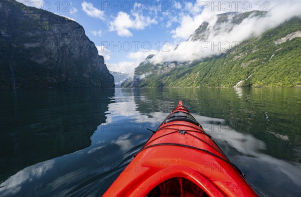 Kayak trip on the Geirangerfjord, tip of a red kayak in the fjord with reflection, atmospheric fjord landscape, first person view at Geiranger, Møre og Romsdal, Norway, Europe