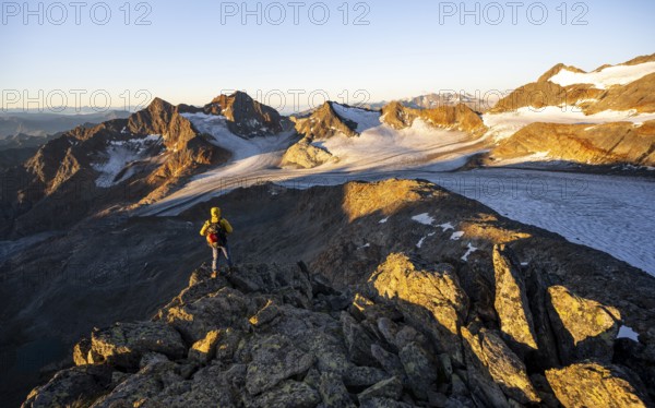 Mountaineers in front of a picturesque high mountain landscape at sunrise with alpenglow, glacier and rocky mountain peaks in the morning light, view at the Becher on mountain peak Königshofspitz and glacier Übeltalferner, Stubai Alps, South Tyrol, Italy, Europe