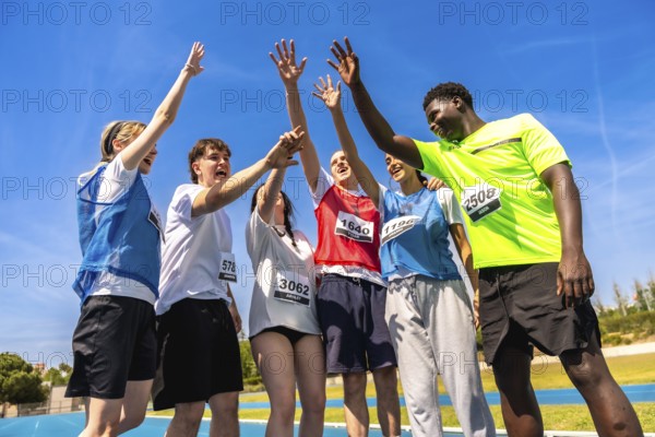 Group of young athletes celebrating their victory on a running track, raising hands together in a display of teamwork and sportsmanship