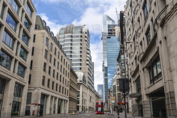 Red double decker bus driving on empty street surrounded by modern and historic buildings in city of london, united kingdom