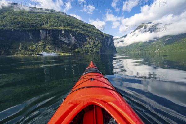 Kayak trip on the Geirangerfjord, tip of a red kayak in the fjord with reflection, atmospheric fjord landscape, first person view at Geiranger, Møre og Romsdal, Norway, Europe