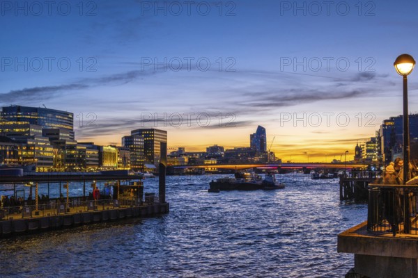 Tugboats sailing on thames during sunset with london's illuminated skyline reflecting on the water