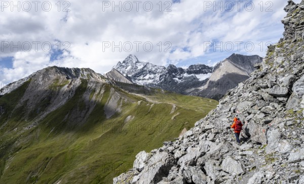 Mountaineer on steep rocky hiking trail, descent from the summit of Kastenegg, view of picturesque mountain landscape with snow-covered summit of the Großglockner, Wiener Höhenweg, Schober group, Hohe Tauern National Park, Carinthia, Austria, Europe