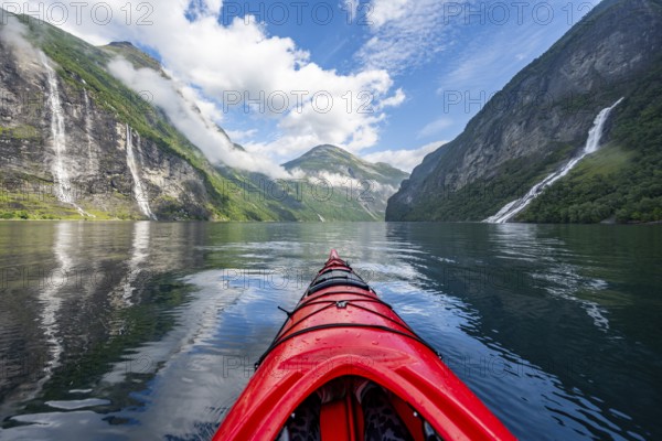 Kayak trip on the Geirangerfjord with waterfall The Seven Sisters and Freier Waterfall, tip of a red kayak in the fjord, atmospheric fjord landscape with reflection, first person view, near Geiranger, Møre og Romsdal, Norway, Europe
