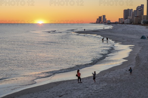 People walking and playing on the beach as the sun sets over the Gulf of Mexico at Gulf Shores, Alabama