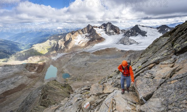 Mountaineer with helmet on a rope-insured path, in high mountain landscape, view of blue glacier lakes, mountain peaks Königshofspitz and Hofmannspitze with glacier of the Übeltalferner, Stubai Alps, South Tyrol, Italy, Europe