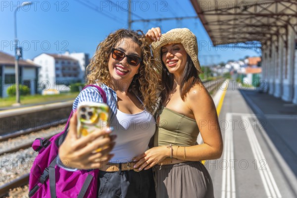Two female tourists taking a selfie with smartphone on a train station platform during summer vacation