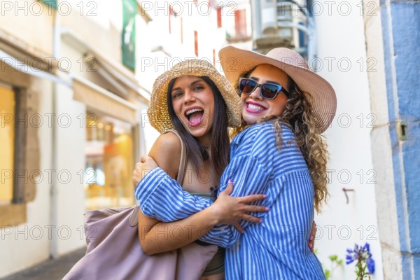 Two cheerful women tourists wearing summer hats are embracing on a city street during their vacation
