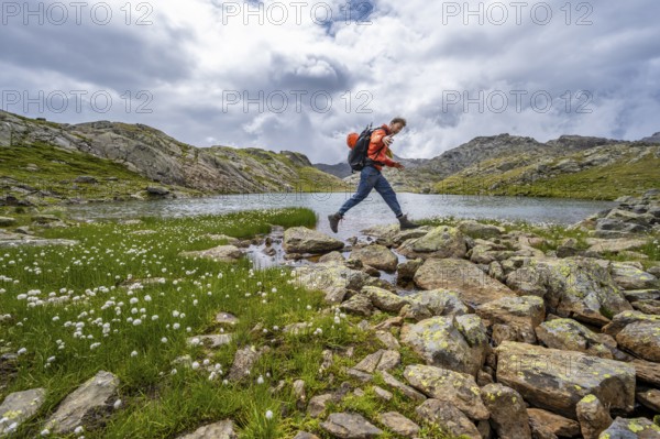 Mountaineer jumping from stone to stone, at a mountain lake in high mountain landscape at the Obere Senner Egete, Seven Lakes Hike, Stubai Alps, near Ridnaun, South Tyrol, Italy, Europe
