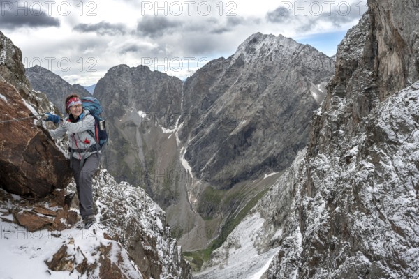 Female mountaineer on a rope-secured climb in a steep rocky mountain landscape with fresh snow in summer, behind mountain peaks Großer Friedrichskopf and Georgskopf, ascent to Hornscharte, Schobergruppe, Hohe Tauern National Park, Carinthia, Austria, Europe