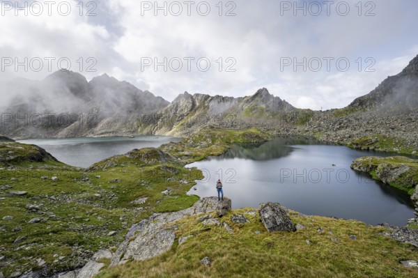 Mountaineer on a rock in front of mountain lakes Wangenitzsee and Kreuzsee, cloudy mountain peaks in the morning, Schober group, Hohe Tauern National Park, Carinthia, Austria, Europe