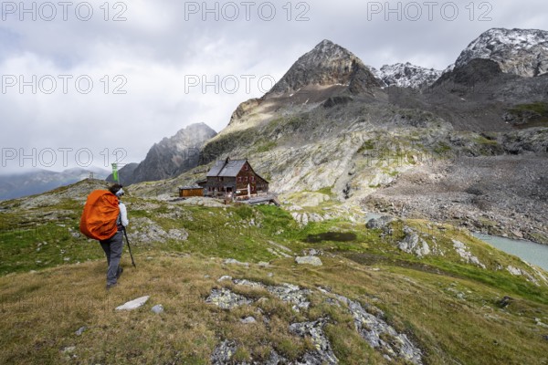 Mountaineer in front of mountain hut Adolf-Nossberger-Hütte, mountain landscape with rocky mountain peaks, in the background summit of Petzeck and Kruckelkopf, Schober group, Hohe Tauern National Park, Carinthia, Austria, Europe