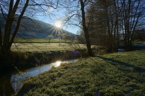 Sunlight breaks through the trees and is reflected in the stream of a tranquil landscape, Kirchzell, Amorbach, Odenwald, Bavaria, Germany, Europe