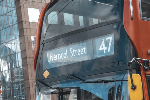 Red double decker bus number 47 showing liverpool street destination, reflecting modern buildings in its windows, in the city of london