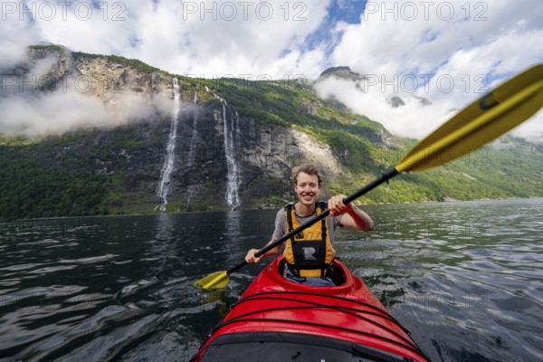 Kayak trip on the Geirangerfjord at the waterfall The Seven Sisters, Young man paddling in a kayak, atmospheric fjord landscape, near Geiranger, Møre og Romsdal, Norway, Europe