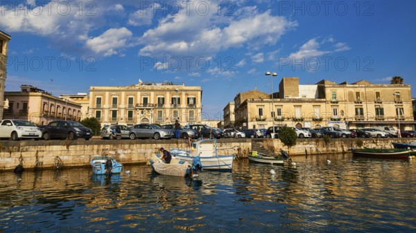 Boats on a waterfront in a town in the warm light and under a blue sky, boat trip around the island of Ortigia, Isola di Ortigia, Syracuse, Sicily, Italy, Europe