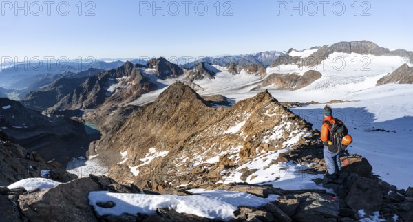 Mountaineer on a rocky ridge on the Wilder Freiger summit, behind him Signal summit and Becher summit with Becherhaus, picturesque high mountain landscape, view of Übeltalferner glacier and rocky mountain peaks Königshofspitz and Sonklarspitze, Stubai Alps, South Tyrol, Italy, Europe