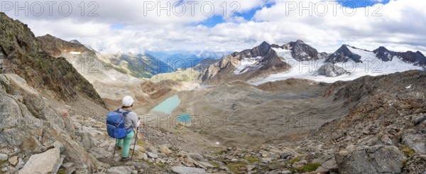 Mountaineer with helmet in high mountain landscape, view of blue glacial lakes, mountain peaks Königshofspitz and Hofmannspitze with glacier of the Übeltalferner, Stubai Alps, South Tyrol, Italy, Europe