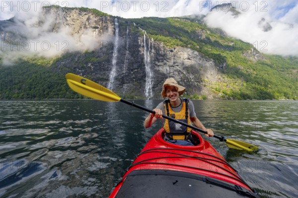 Kayak trip on the Geirangerfjord at the waterfall The Seven Sisters, Young man paddling in a kayak, atmospheric fjord landscape, near Geiranger, Møre og Romsdal, Norway, Europe