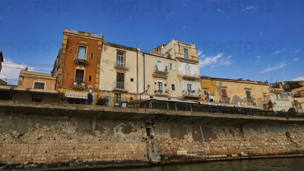 Houses with different facades on a stone coastal wall under a sunny sky, boat trip around the island of Ortigia, Isola di Ortigia, Syracuse, Sicily, Italy, Europe