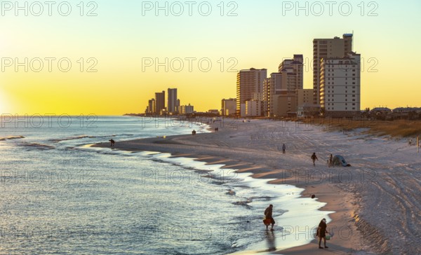 People walking and playing on the beach as the sun sets over the Gulf of Mexico at Gulf Shores, Alabama
