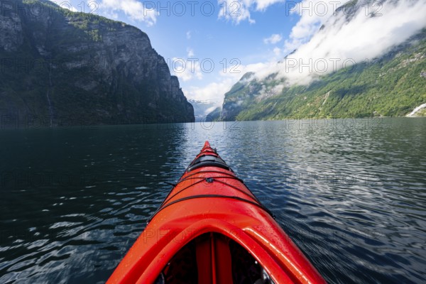 Kayak trip on the Geirangerfjord, tip of a red kayak in the fjord with reflection, atmospheric fjord landscape, first person view at Geiranger, Møre og Romsdal, Norway, Europe