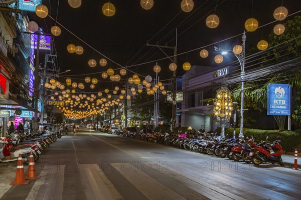 Scooters and motorcycles under lighted spheres strung across downtown street in Chiang Rai, Thailand, Asia