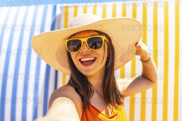 Young woman with sunhat and sunglasses taking a selfie on a striped background at the beach during summer vacation