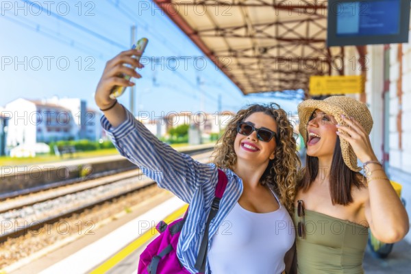 Two happy female tourists taking a selfie with a smartphone at a train station before departure