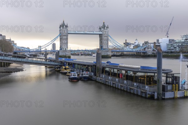 Tower bridge standing majestically over the river thames with boats moored at a pier, showcasing the iconic london landmark